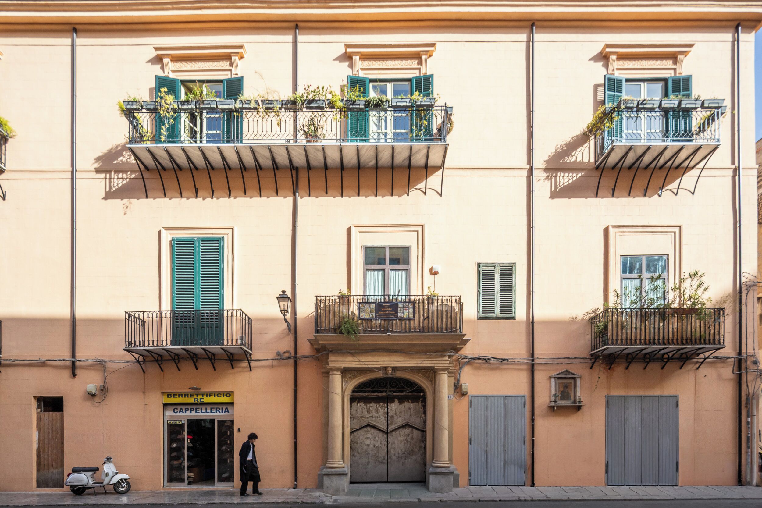Un edificio con una tienda en la planta baja, balcones adornados con plantas y el toldo de la tienda cerrado.