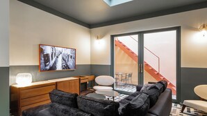 Una sala de estar moderna con un sofá, una mesa de centro, un televisor montado en la pared y una escalera que da a un espacio exterior.