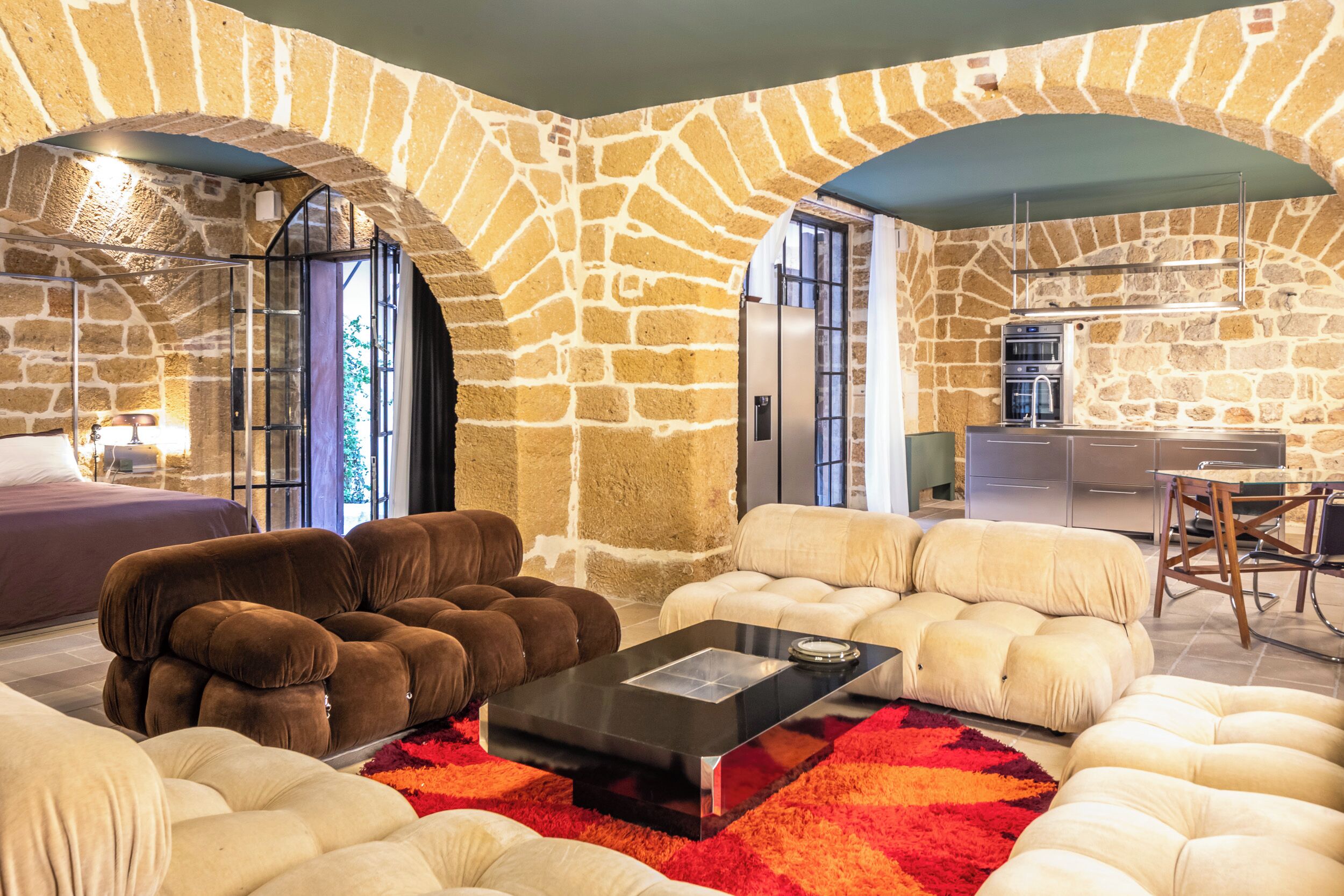 A modern living room with stone walls, a sofa set, a coffee table, and a kitchen area with an oven.