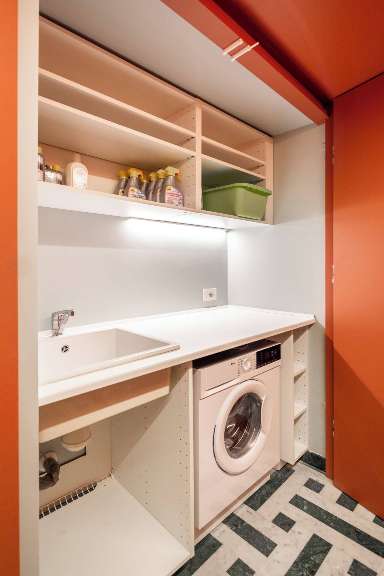Une petite buanderie équipée d’un lave-linge, d’un évier et d’étagères pour le rangement.