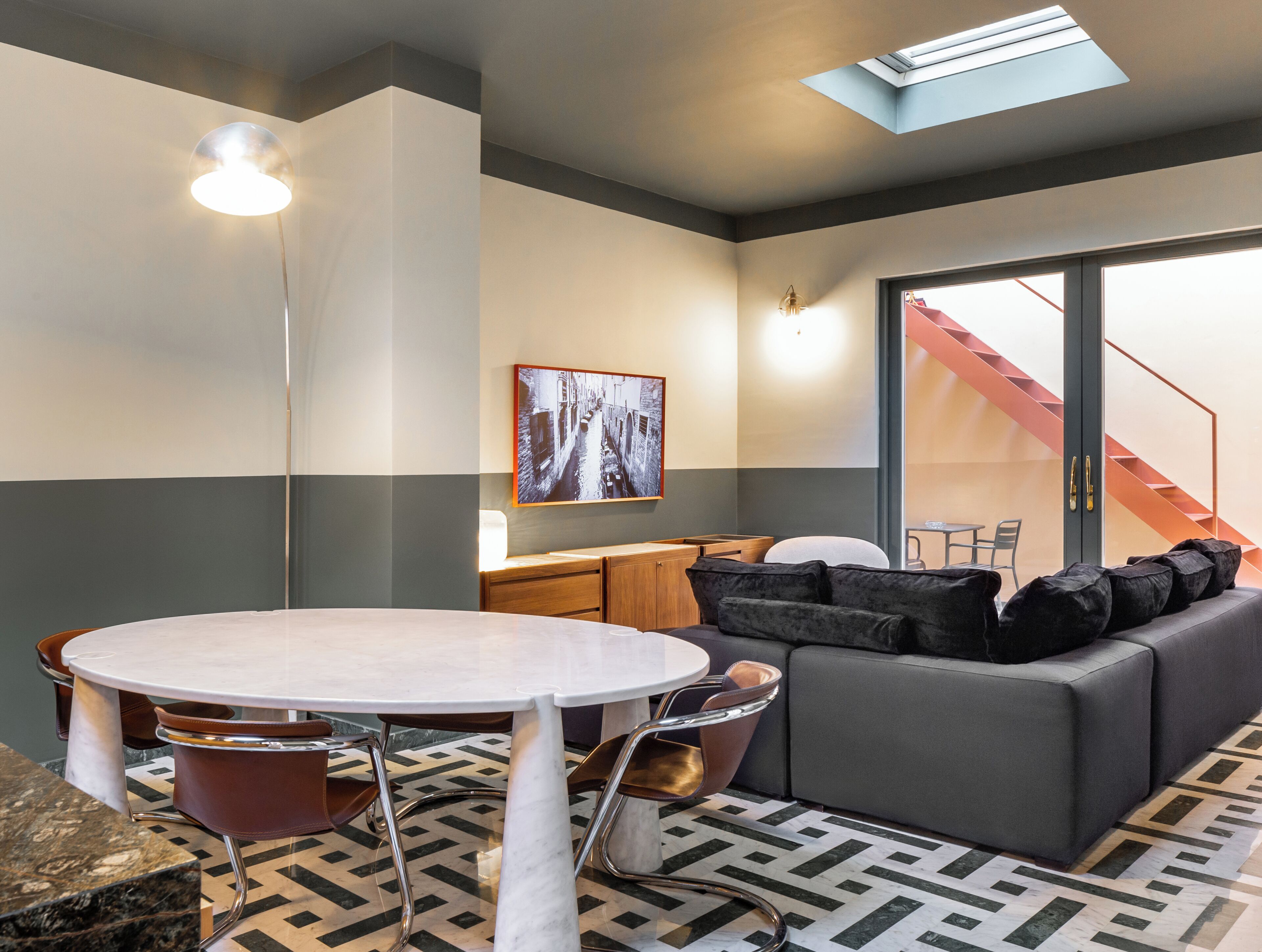 A modern interior with a round table, chairs, a sofa, and a staircase.