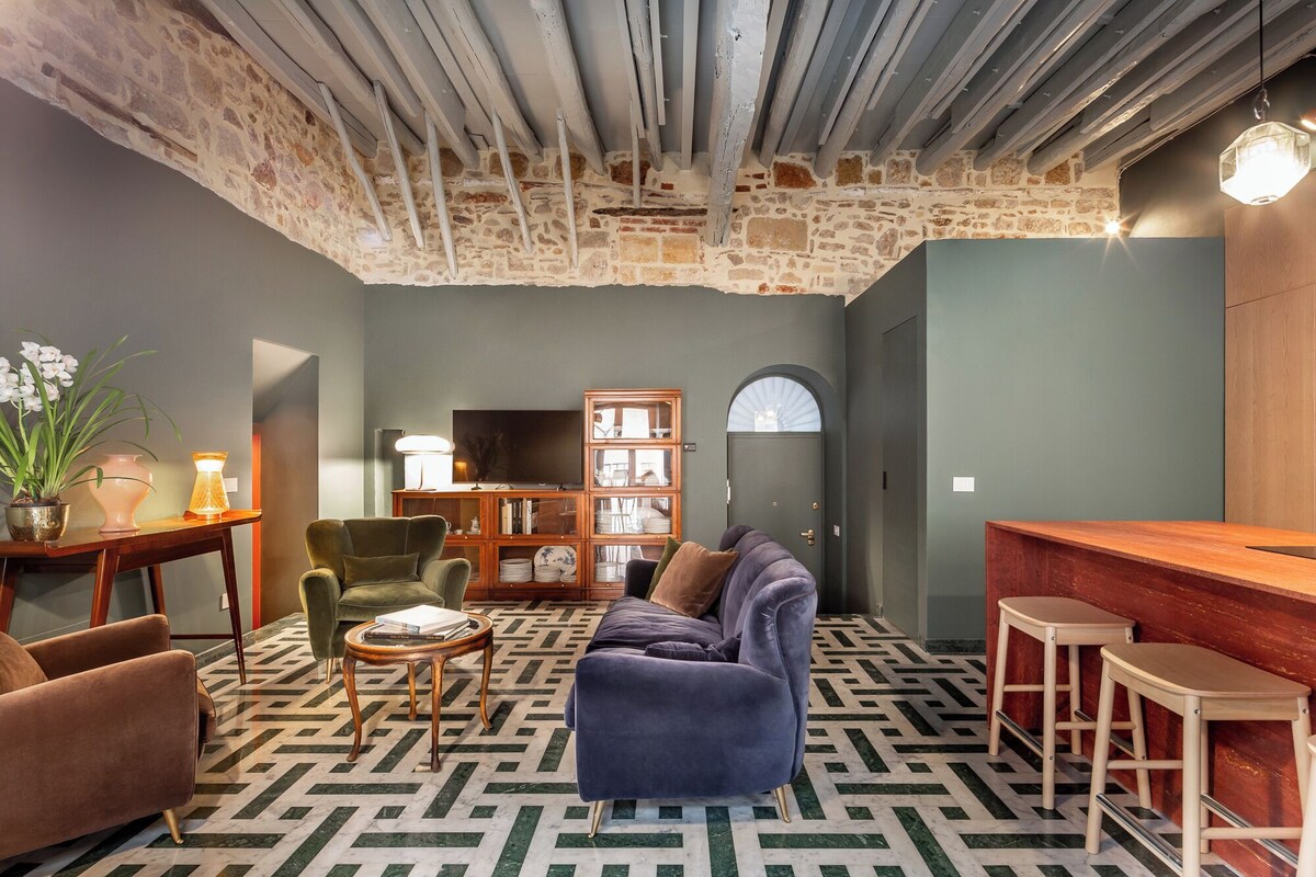 A cozy living room with a stone wall, a wooden ceiling, a sofa, a TV, and a patterned floor.
