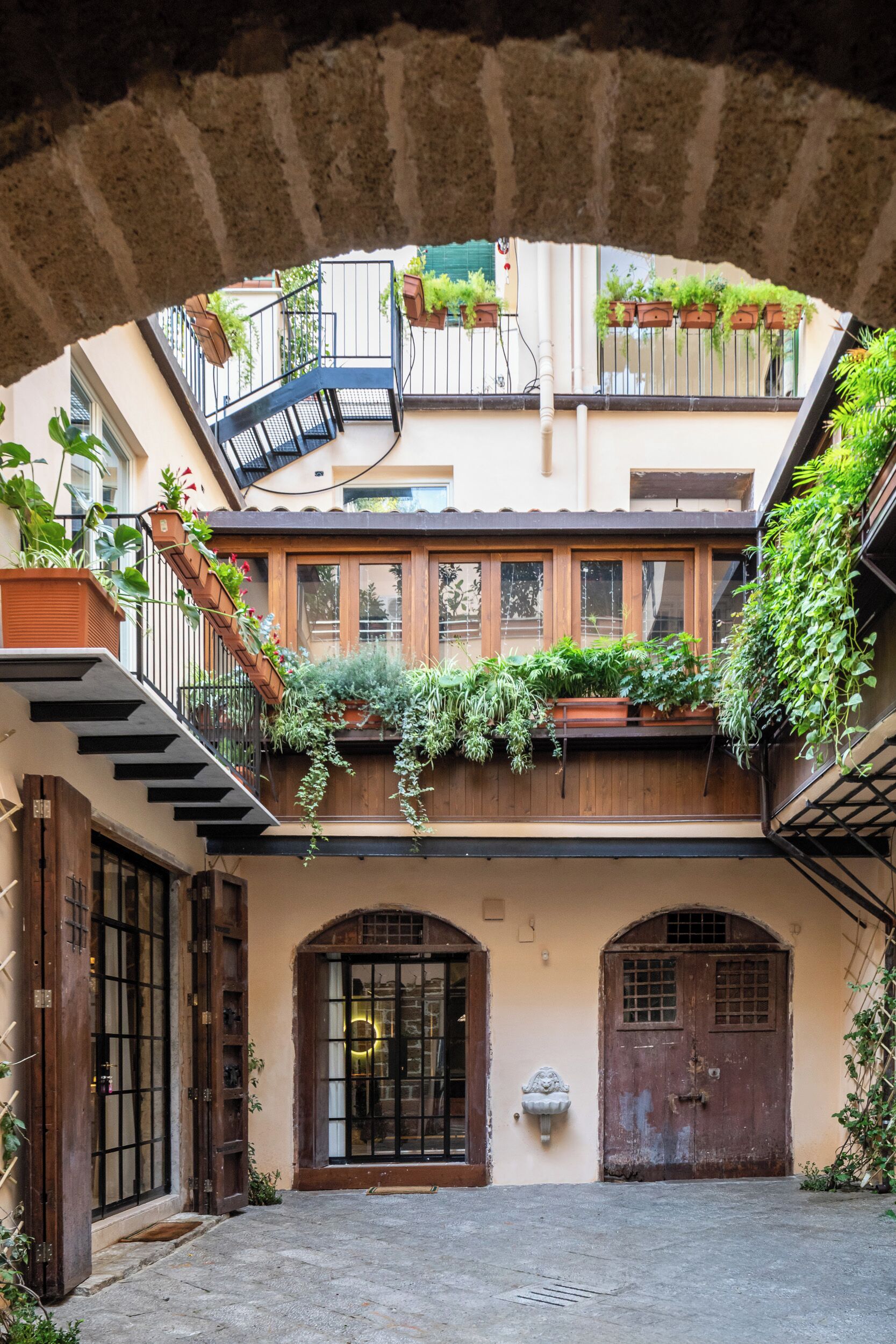 Une cour avec un escalier, des portes en bois et des plantes en pot.