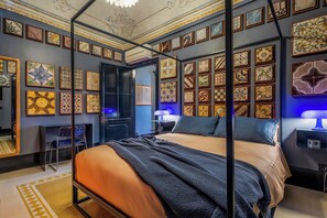A room with a four-poster bed, a desk, and a chair. The walls are decorated with framed tiles. - Le stanze al genio di Darlon (Palermo)