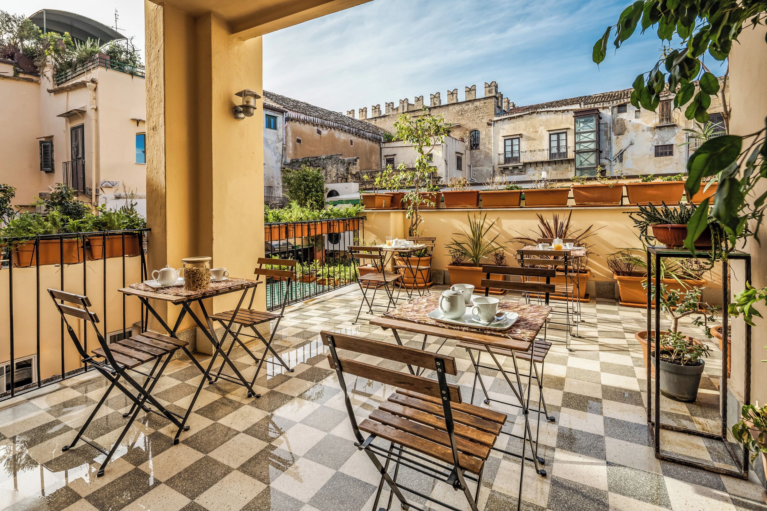 Una terraza con suelo a cuadros, mobiliario exterior y plantas en macetas.
