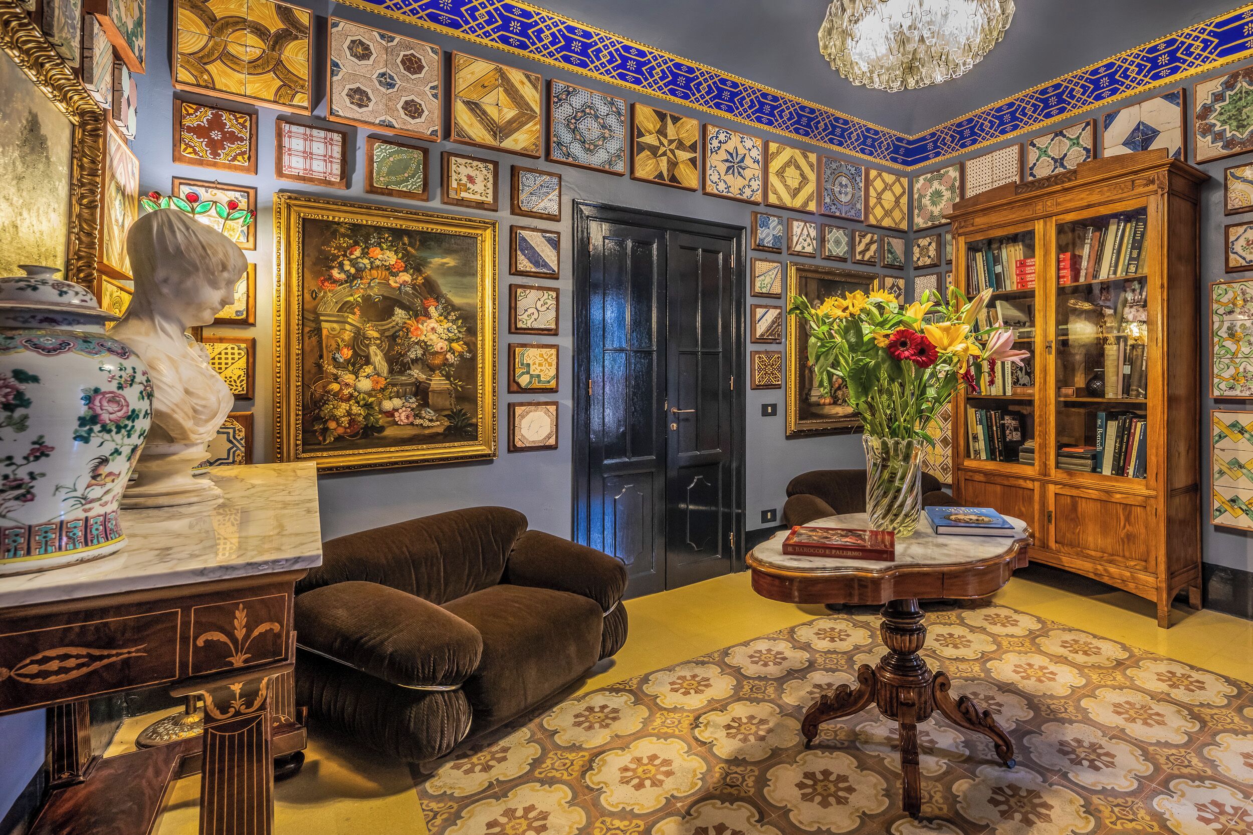 A room with a marble table, a bust sculpture, a sofa, a bookshelf, and a patterned floor.