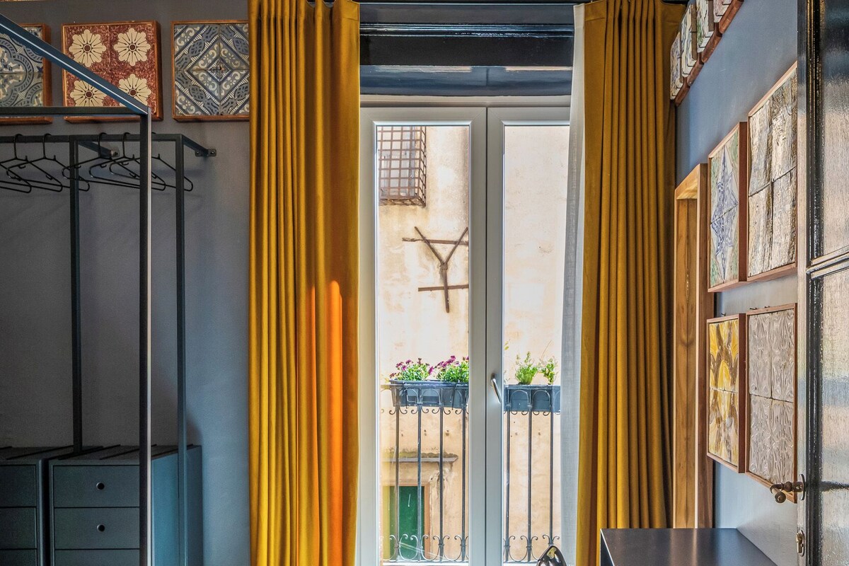 A hotel room with a bed, a desk, a wardrobe, and a balcony with plants.