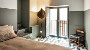Un dormitorio con cama, una silla, un ventanal grande y una puerta que da a un balcón al aire libre.