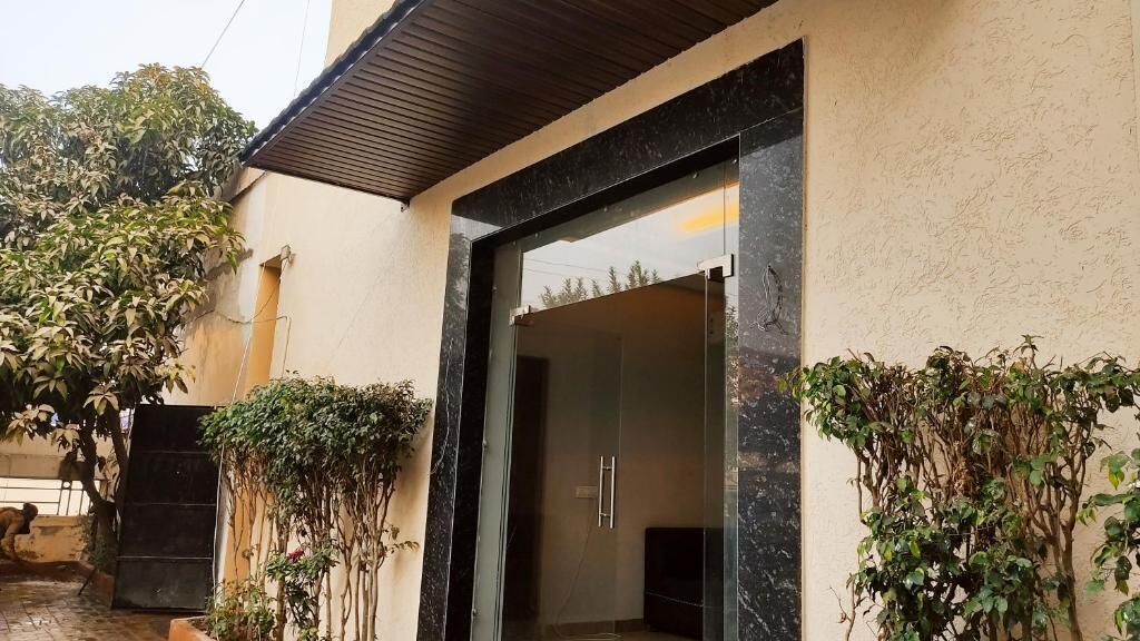 Entrada de un edificio moderno con puerta de vidrio, reja metálica y pared de concreto.