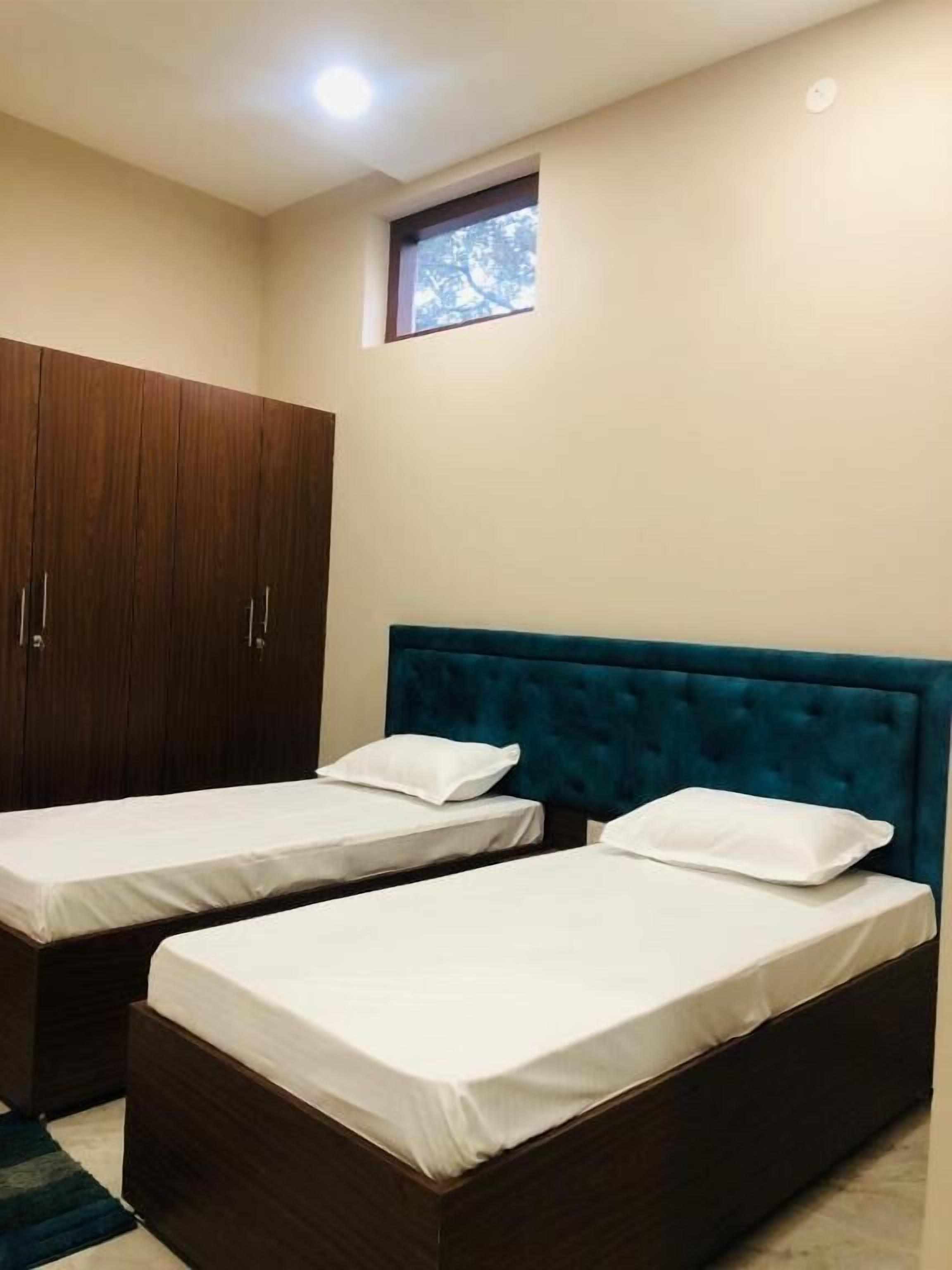 A room with two single beds, a wooden wardrobe, and a small window.