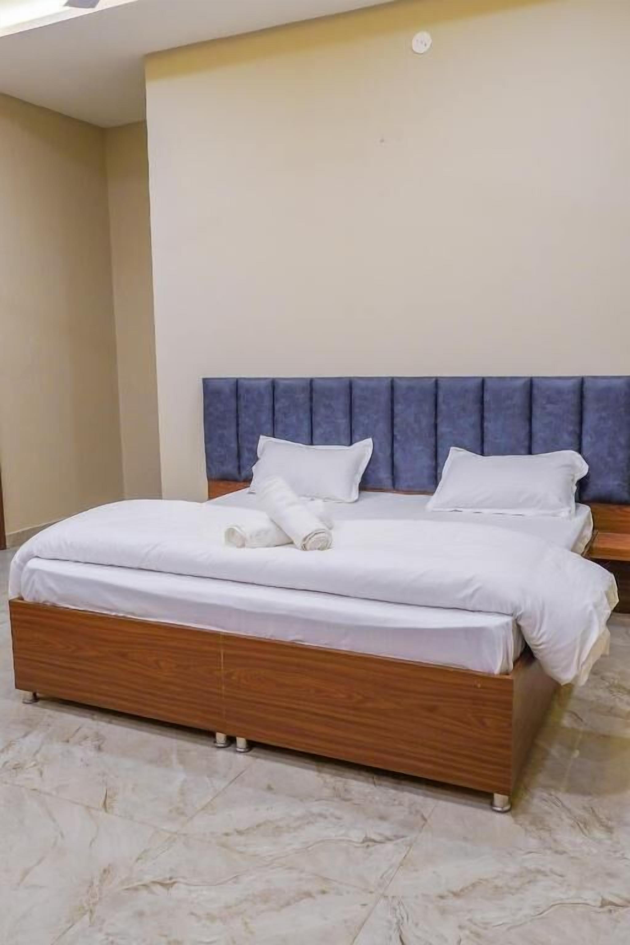A double bed with a wooden frame and a blue headboard, white bedding, and a marble floor.