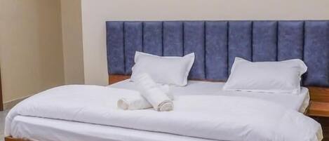 A double bed with a wooden frame and a blue headboard, white bedding, and a marble floor.