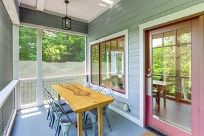 A covered porch with a wooden table and chairs, large windows, and a red door. - Spacious Home w/ Hot Tub & Views in Black Mountain (Black Mountain)