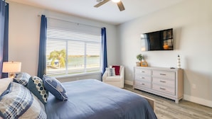 Ein Schlafzimmer mit Bett, Kommode, Fernseher und einem Fenster mit Vorhängen.