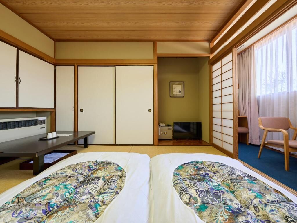 A traditional Japanese-style room with tatami flooring, a futon bed, a desk with a chair, and sliding doors.