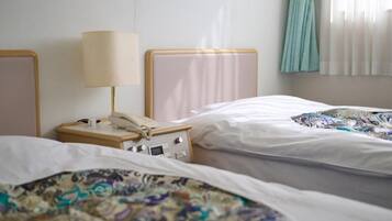 Habitación de hotel con dos camas, una mesita de noche con lámpara y una ventana con cortinas.