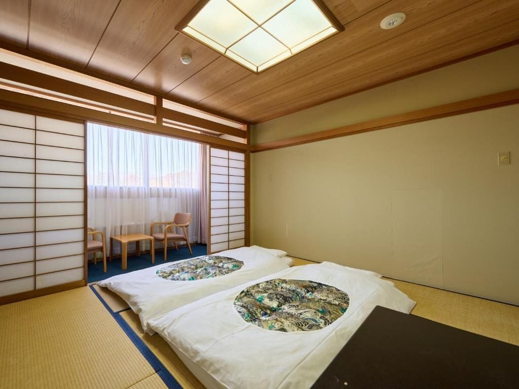 A traditional Japanese room with tatami flooring, a shoji screen, and a futon bed with a patterned blanket.