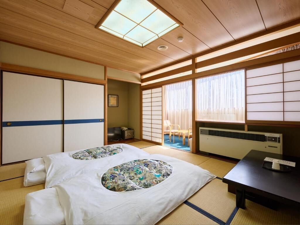 Una habitación japonesa tradicional con suelo de tatami, una cama futón, puertas correderas y vistas a través de biombos shoji.