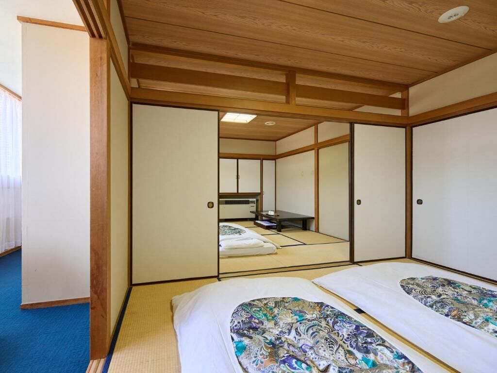 Une pièce de style japonais traditionnel, avec un sol recouvert de tatamis, des portes coulissantes et un lit agrémenté de draps à motifs.