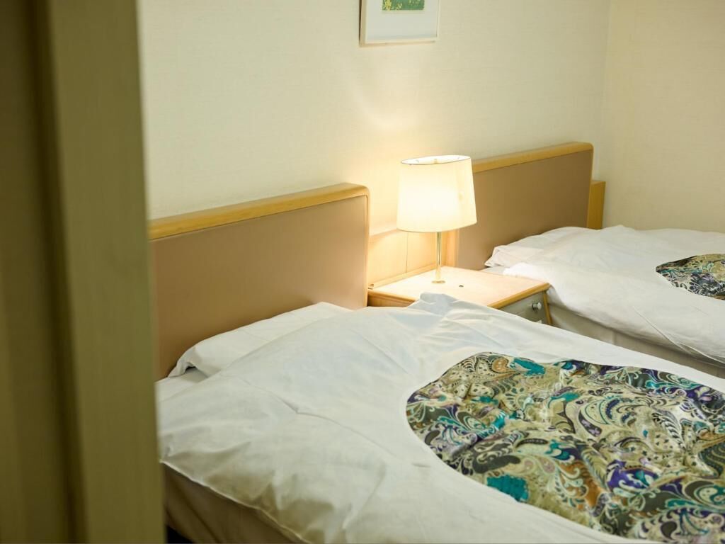 Habitación de hotel con dos camas, cada una con ropa blanca, una mesita de noche con lámpara y un cuadro en la pared.