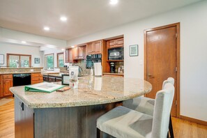 A kitchen with granite countertops, wooden cabinets, a built-in microwave, and a large island with seating.