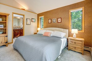 Ein Schlafzimmer mit einem großen Bett, Nachttischen, einer hölzernen Kommode und einem Fenster mit Blick auf Bäume.