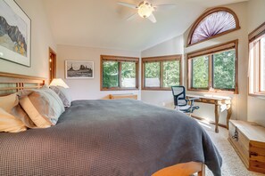 Ein Schlafzimmer mit einem Bett, einem Schreibtisch und einem Stuhl. Es gibt Fenster mit Jalousien, einen Deckenventilator und Kunstwerke an den Wänden.