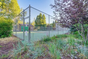 Cancha de tennis tancada per una tanca metàl·lica, envoltada d'arbres i arbustos.