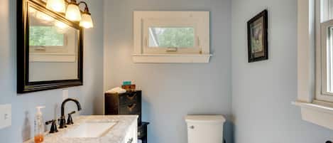 A bathroom with a sink, mirror, toilet, and window.