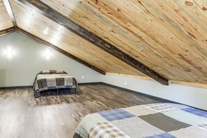 Een kamer met een schuine kap, een bed met quilt en een klein tafeltje.