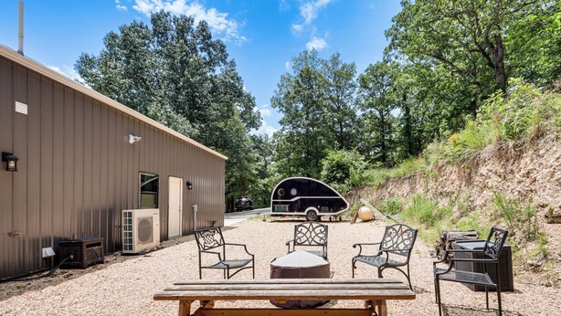 Un espace extérieur aménagé avec un banc et des chaises, une table de pique-nique couverte, et un véhicule récréatif en arrière-plan.