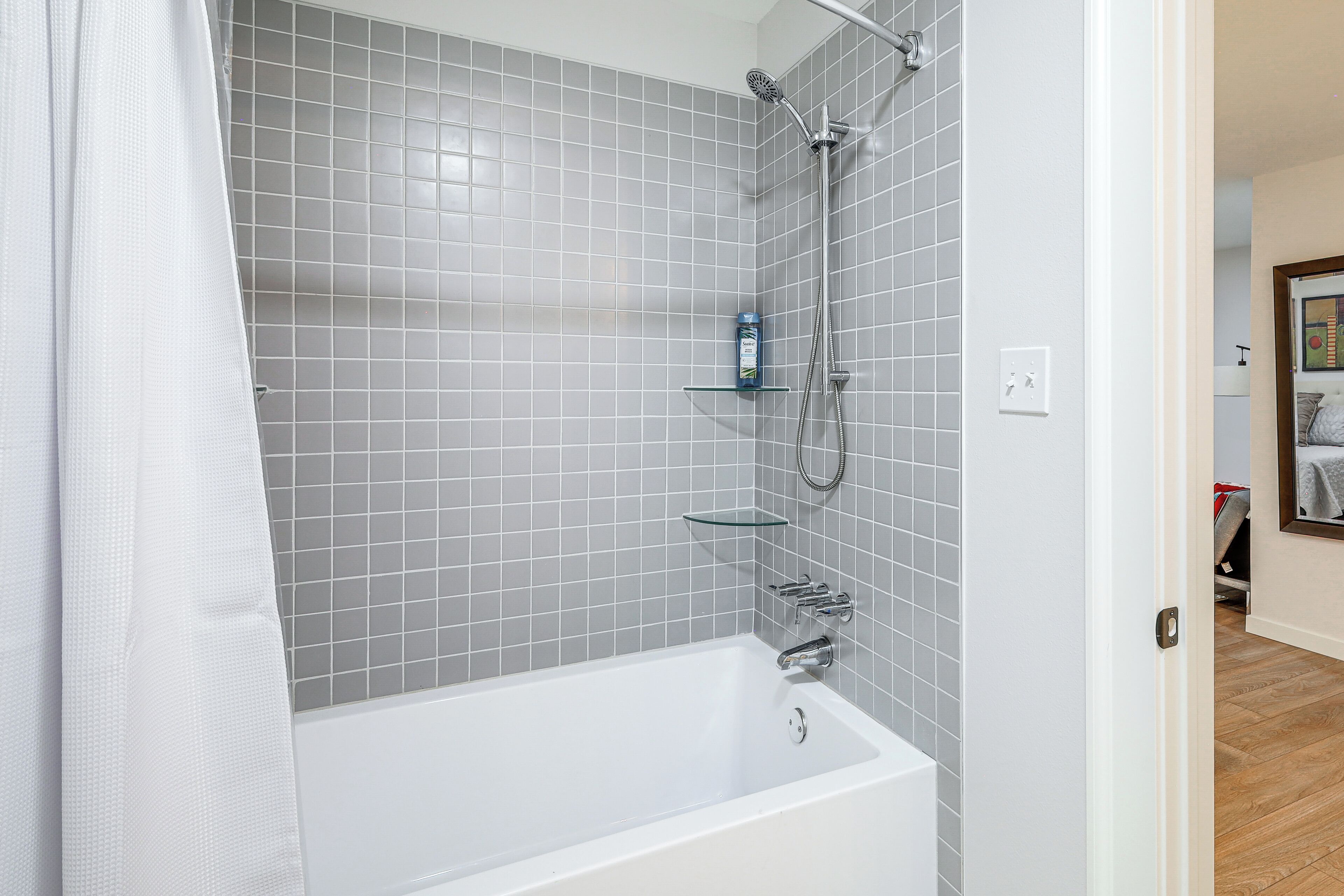 A modern bathroom with a white bathtub, grey tiled walls, and a shower area.