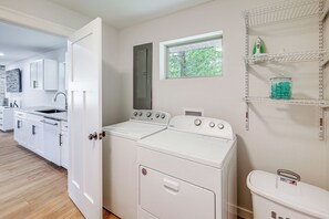 A laundry room with a washer and dryer, a window, and a shelf with bottles. - Lake-View Deck! Modern Greers Ferry Lake Retreat (Higden)