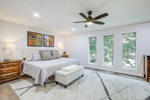 A bedroom with a bed, bedside tables, a ceiling fan, and large windows. - Lake-View Deck! Modern Greers Ferry Lake Retreat (Higden)