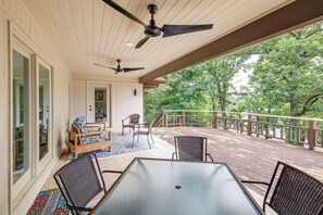A covered outdoor deck with a table and chairs, a ceiling fan, and a view of trees. - Lake-View Deck! Modern Greers Ferry Lake Retreat (Higden)