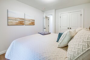 A bedroom with a large bed, two wall-mounted paintings, a door, and a white ceiling. - Lake-View Deck! Modern Greers Ferry Lake Retreat (Higden)