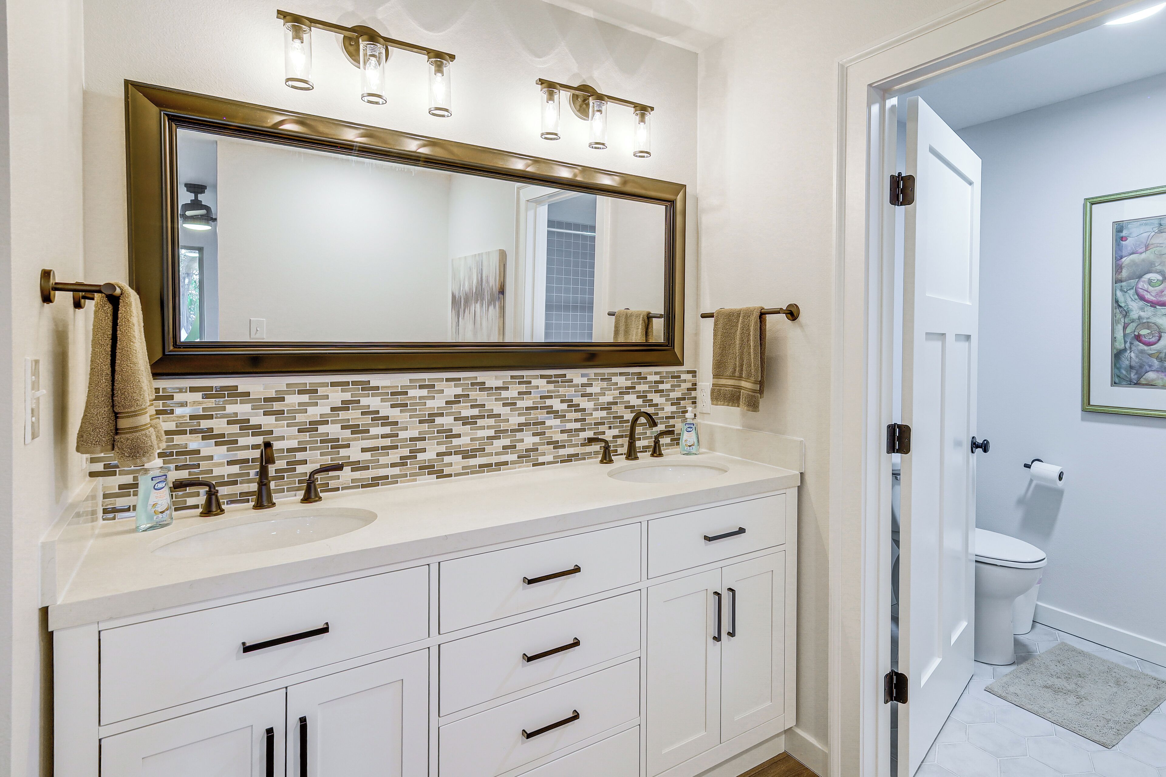A bathroom with a large mirror, two sinks, and a tiled backsplash.