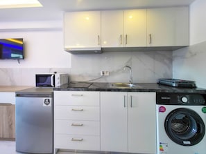 Eine kleine Küche mit Waschmaschine, Mikrowelle und kleinem Kühlschrank.