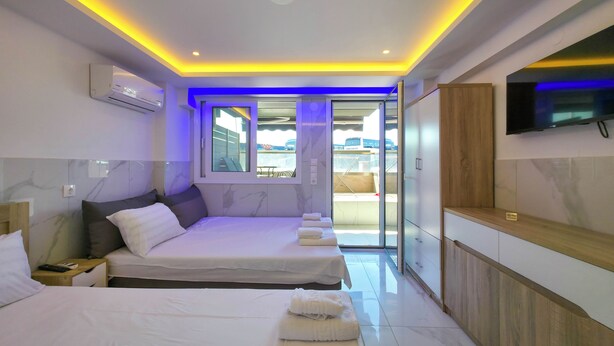 Quarto de hotel com duas camas, televisão, porta de vidro deslizante para uma varanda e aparelho de ar condicionado.
