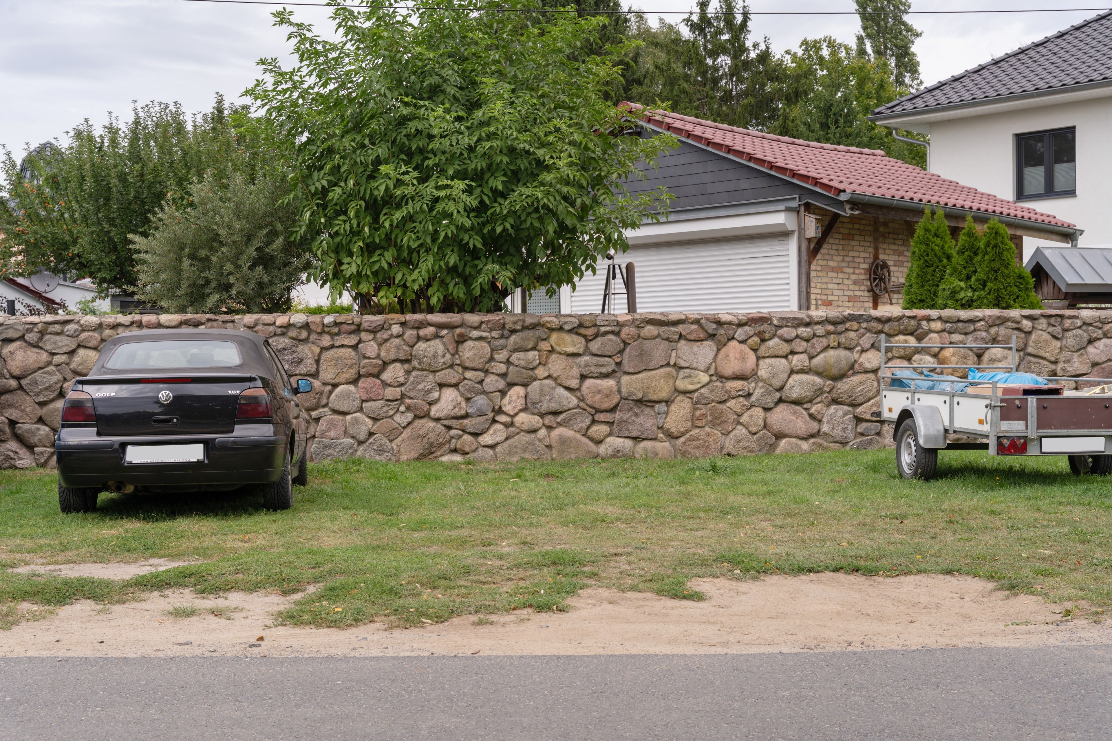 A residential area with a stone wall, a parked Volkswagen Golf, and a trailer.