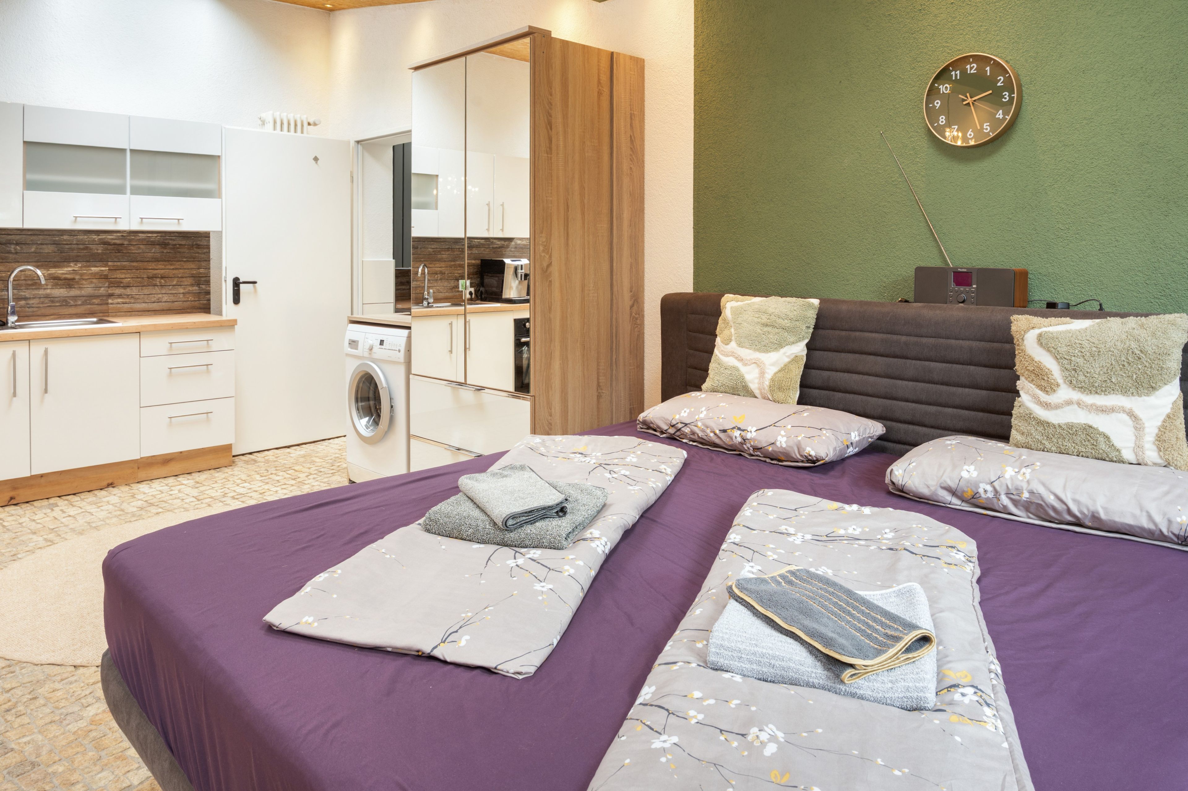 Ein modernes Schlafzimmer mit einem großen Bett, einer integrierten Waschmaschine und einer grünen Wand mit einer Uhr.