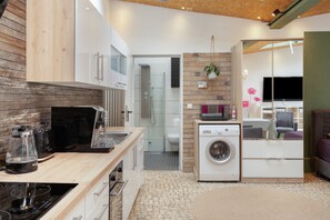 Une cuisine compacte équipée d’appareils modernes, un lave-linge et un petit coin salon avec un téléviseur et des sièges.