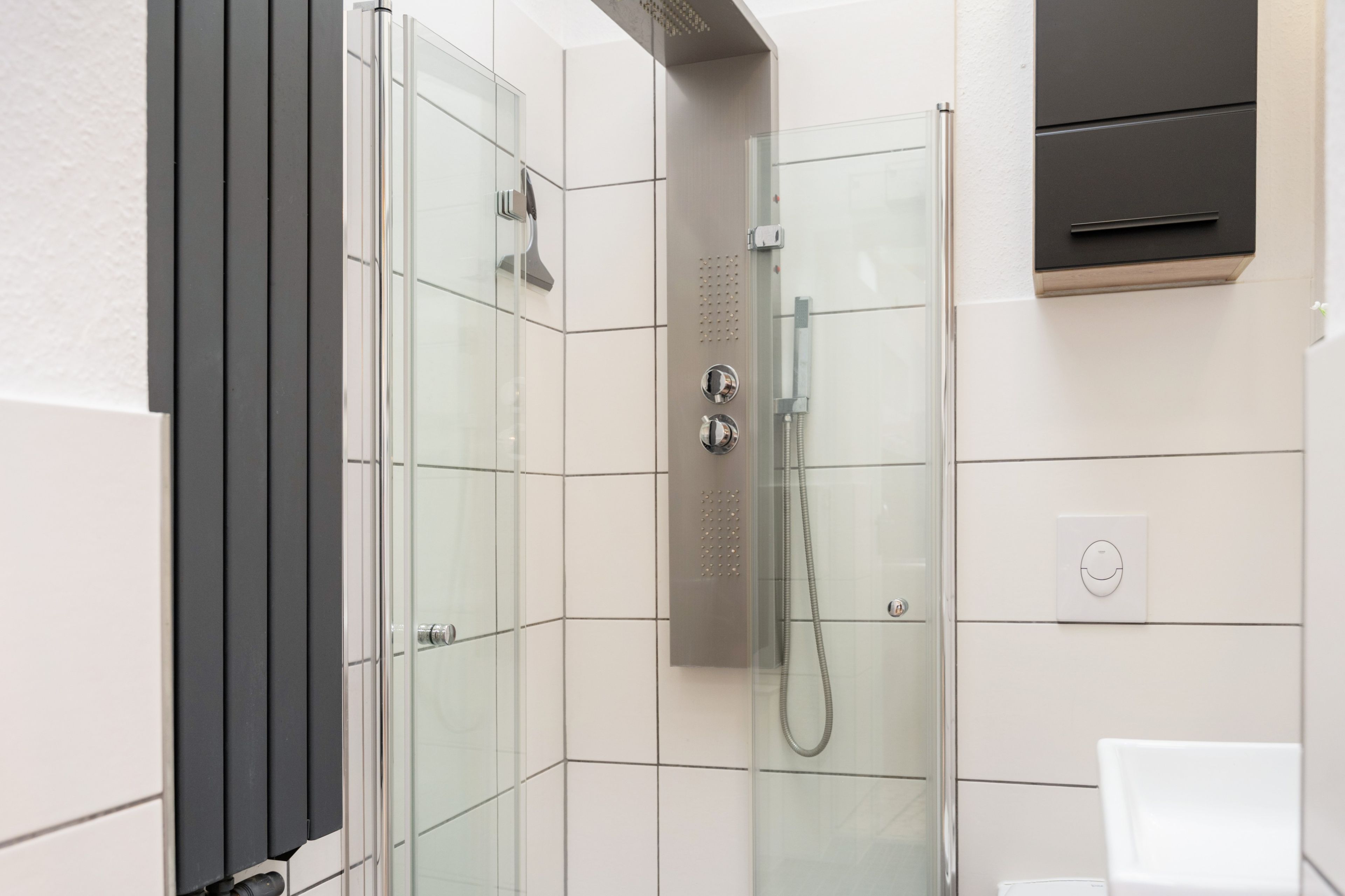 Ein modernes Badezimmer mit einer ein Glas-Duschkabine, einem weißen Waschbecken und einem integrierten Schrank.