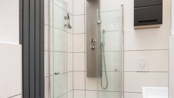 Ein modernes Badezimmer mit einer ein Glas-Duschkabine, einem weißen Waschbecken und einem integrierten Schrank.