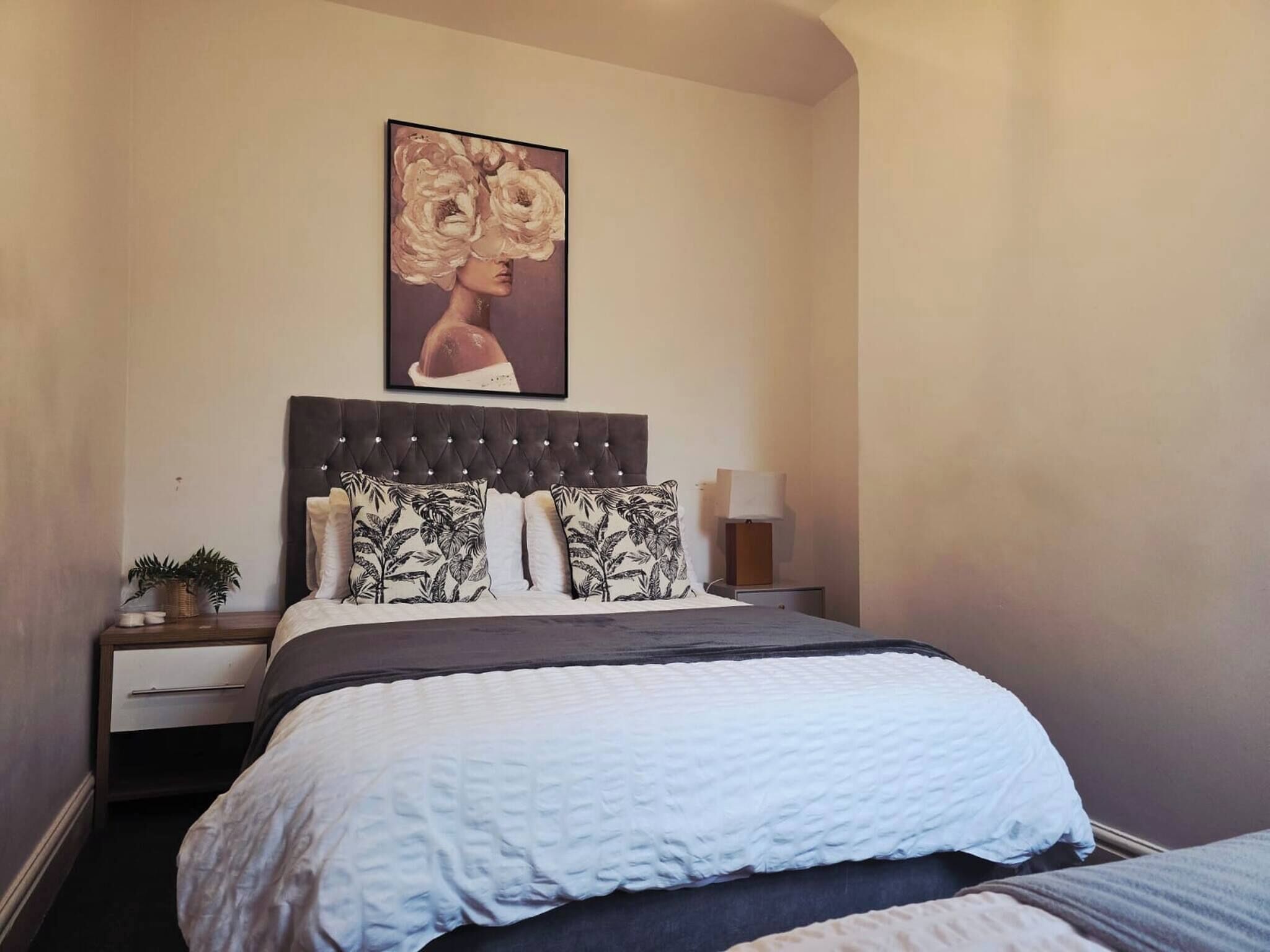 A neatly arranged bedroom with a tufted headboard, a large bed with a white quilt, two nightstands with lamps, and a framed artwork above the bed.