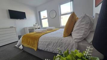 A modern hotel room with a bed, a bedside table, a flat-screen TV, and a window.