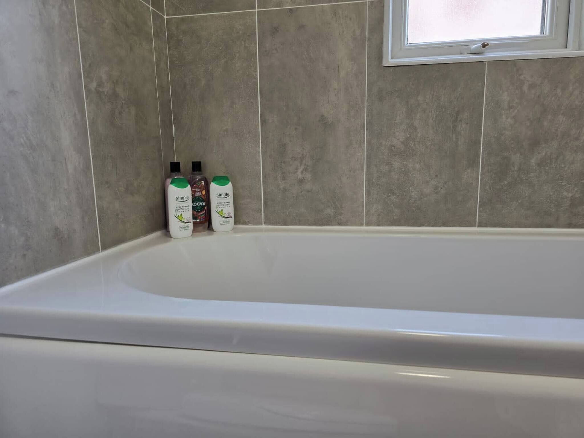 Un baño con bañera, paredes de azulejos y tres botellas de champú.
