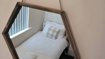 A hexagonal mirror hanging in a room with a bed, pillows, and a window.