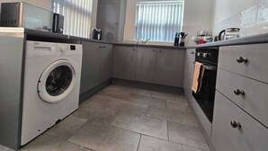 A compact kitchen with a washing machine, a stove, and a sink. - Cozy House in Liverpool (Liverpool)