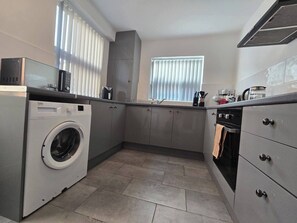 Pieni, käytännöllinen keittiö, jossa on pesukone, liesi ja pesuallas.